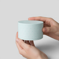 Stockk a light blue cylindrical jewelry box with a removable lid, featuring a subtle polka dot pattern. Made of textured rigid cardboard.