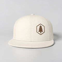 Stockk snapback hat in off-white cotton with a flat brim and a hexagonal patch featuring a brown tree logo.