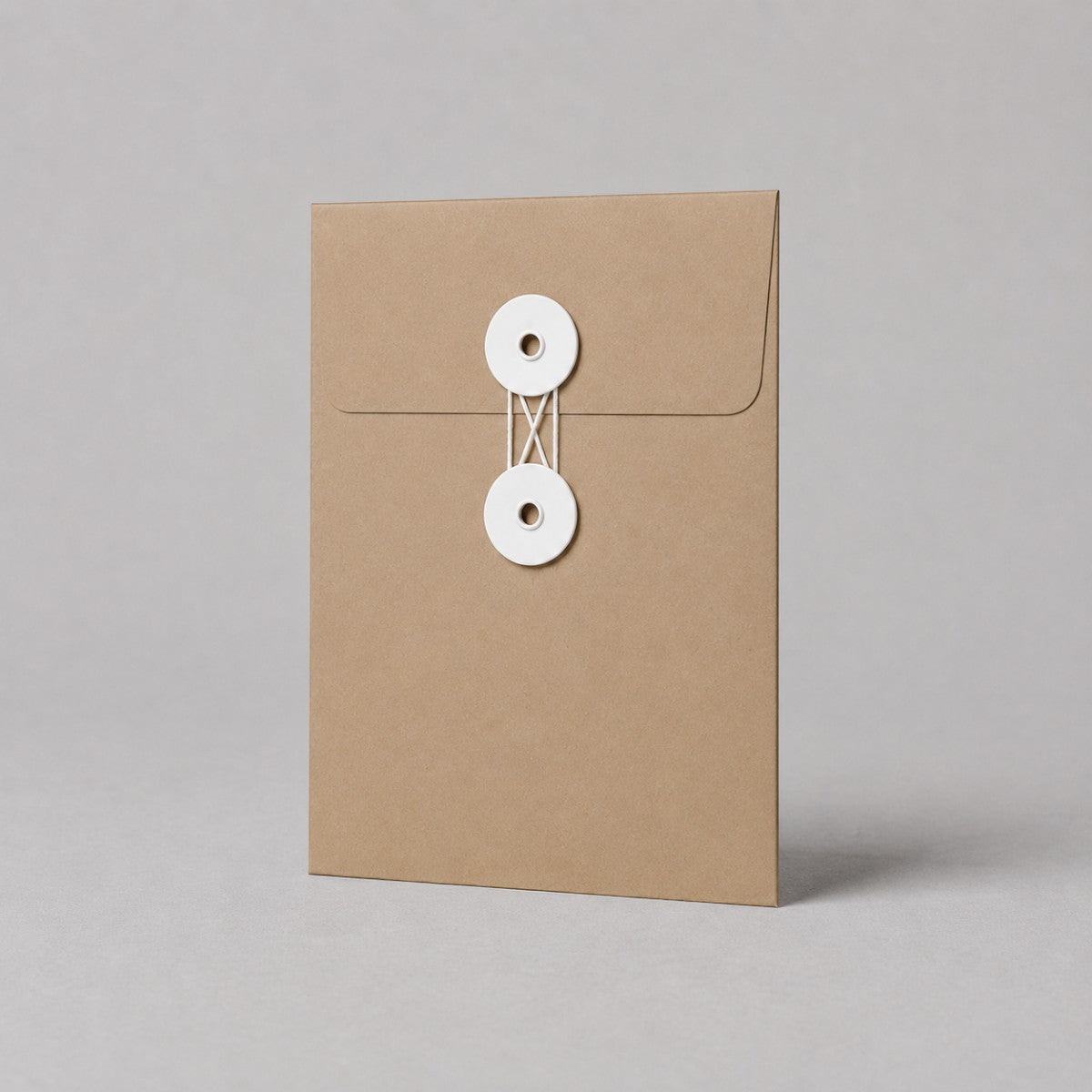 Stockka brown kraft paper envelope with white string and disc closure, ideal for documents and invitations.