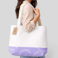 Stockka white canvas tote bag with a purple graphic design on the bottom and long handles, worn by a woman.
