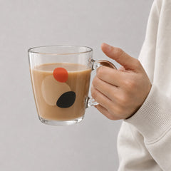 Stockka clear glass mug with a wide shape and modern abstract red, beige, and black circular print, held by hand.