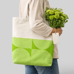 Stockka natural cotton canvas tote bag with a geometric lime green pattern on the bottom half. A person holds the bag with a bouquet of green flowers.