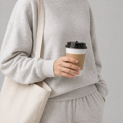 Stockka double-walled paper coffee cup with black lid and kraft paper sleeve, held by a person in loungewear.