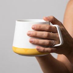 Stockka modern ceramic mug with a white and yellow geometric design and a unique angular handle held in a hand