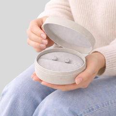 Stockka light grey round jewelry box with removable lid, holding diamond stud earrings. Made of rigid cardboard with matte finish.