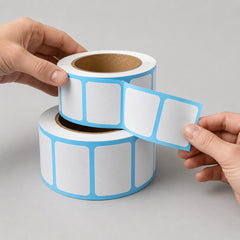 Stockka white square labels with rounded corners on a roll, featuring a light blue border. Ideal for product marking, packaging, and shipping.