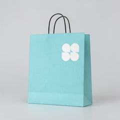 Stockka tall turquoise paper shopping bag with thin rope handles and a white four-petal logo.