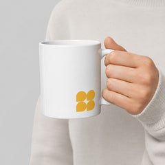 Stockka classic white ceramic mug with a yellow geometric logo held by a person in a beige sweater