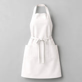 Stockka white full-length apron with two side pockets, adjustable neck strap, and waist tie. Made from a cotton-polyester blend.