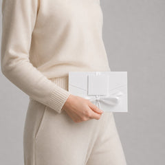 Stockka premium white paper gift envelope with satin ribbon and blank tag, held by a person in a cream sweater and pants.