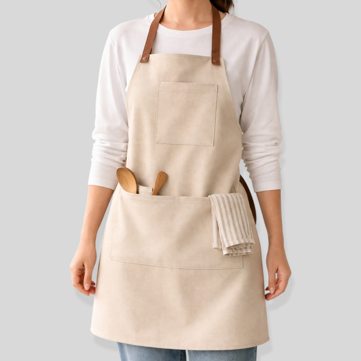 Stockka full length beige cotton-polyester blend apron with two pockets and leather straps, ideal for kitchen or workshop use.