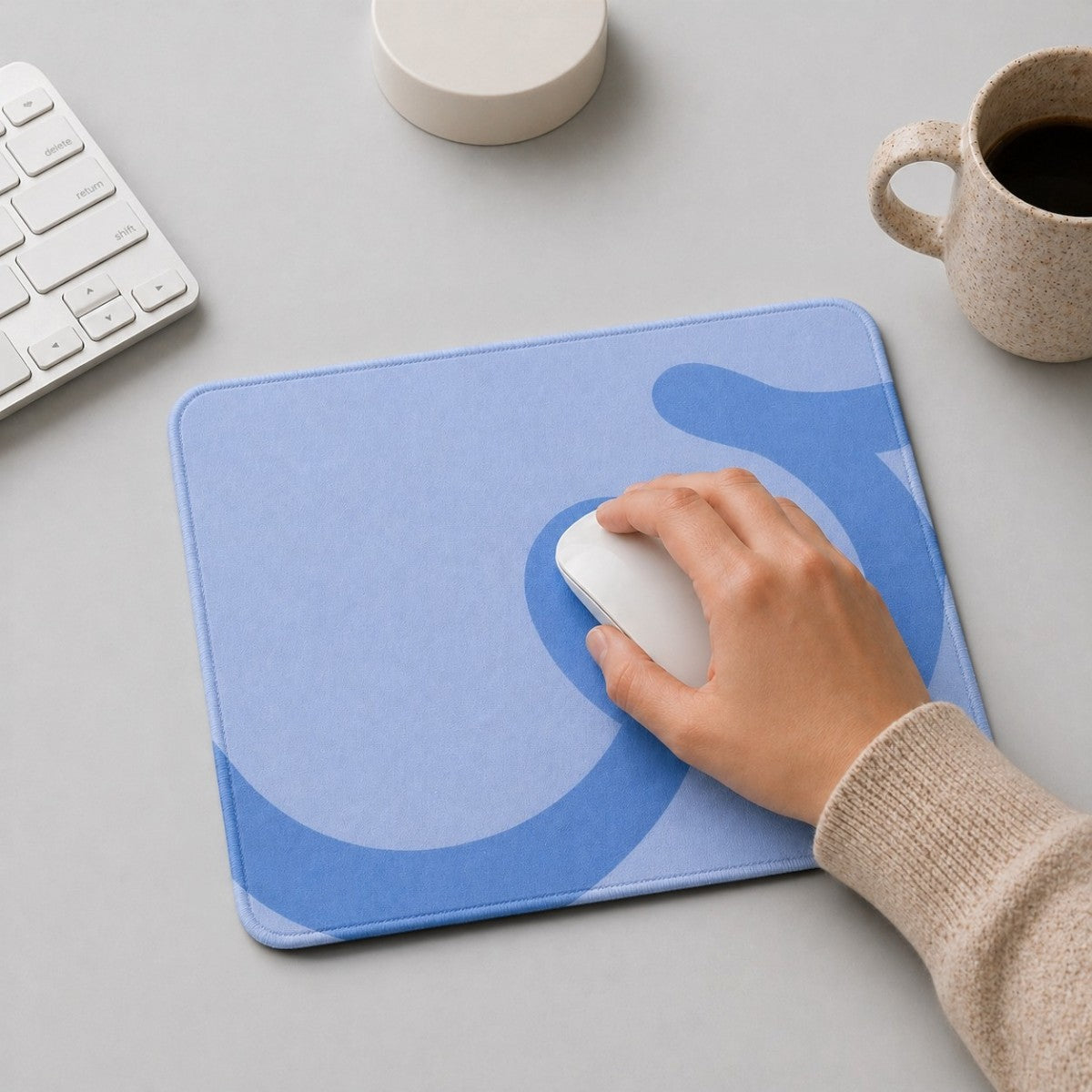 Stockka light blue mousepad with rounded corners and a subtle darker blue abstract design. A hand uses a white mouse on the pad.