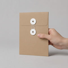 Stockka brown kraft paper envelope with white string and disc closure, ideal for documents and invitations.