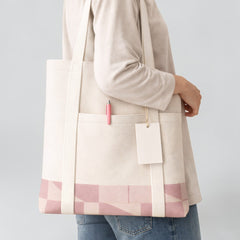Stockka canvas tote bag with front pocket and long shoulder straps, featuring a pink geometric pattern at the base.