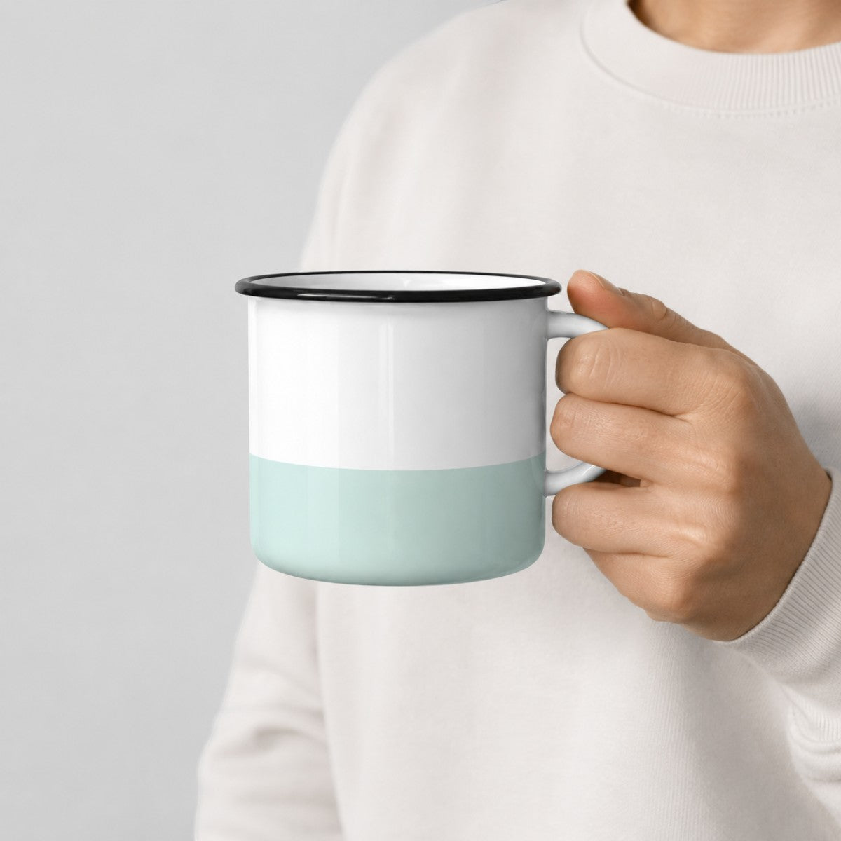 Stockka ceramic camping-style mug in white and mint green with a black rim held in a hand