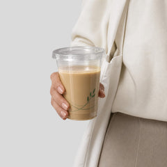 Stockka clear PET plastic cup with flat lid, holding iced coffee or smoothie. Features subtle green leaf design.