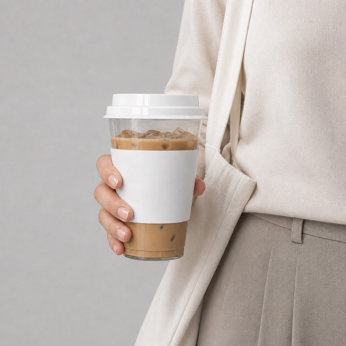 Stockka clear plastic cup with white cardboard sleeve and flat lid, holding iced coffee.