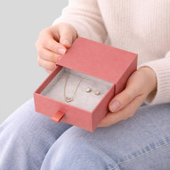 Stockka coral pink jewelry box with drawer, featuring a heart necklace and stud earrings inside on soft grey lining.