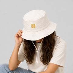 Stockka cream cotton blend bucket hat with gold four-petal flower logo and chin strap, ideal for beach or outdoor activities.