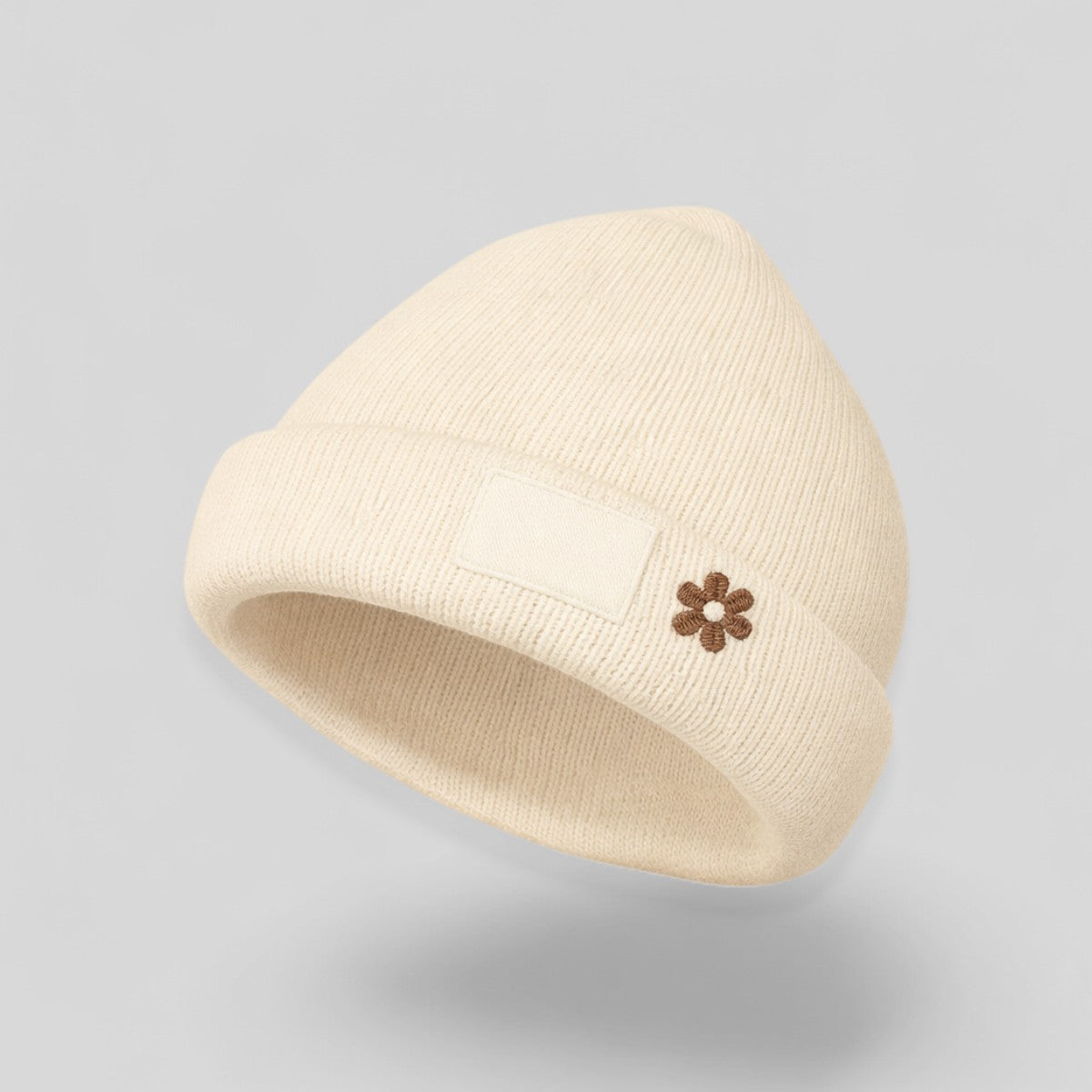 Stockka cream acrylic knit beanie with a small brown flower embroidery and a blank patch.