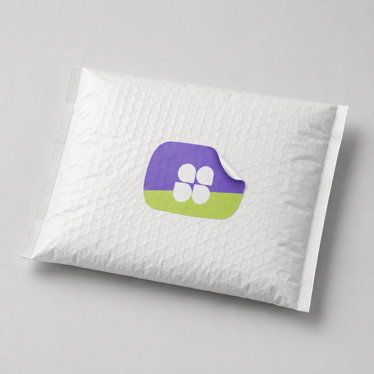 Stockka custom shaped sticker with rounded edges, purple and lime green design with four white shapes. Applied to a white padded envelope.