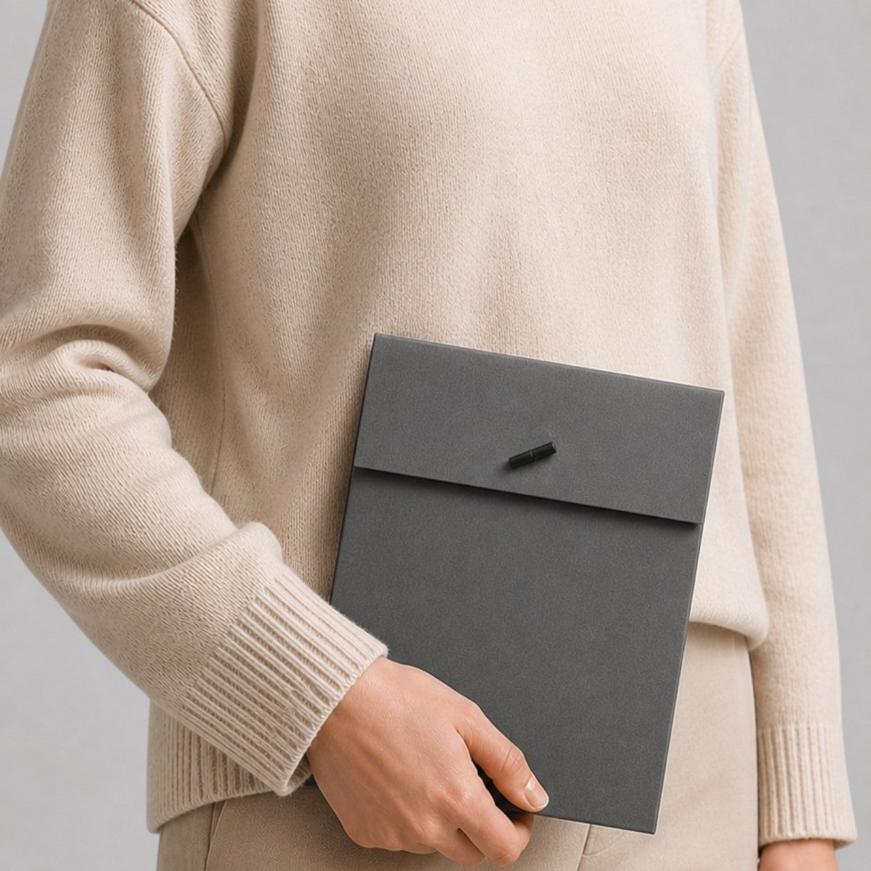Stockka minimalist dark grey paper presentation folder with tab closure, held by a person in a beige sweater.