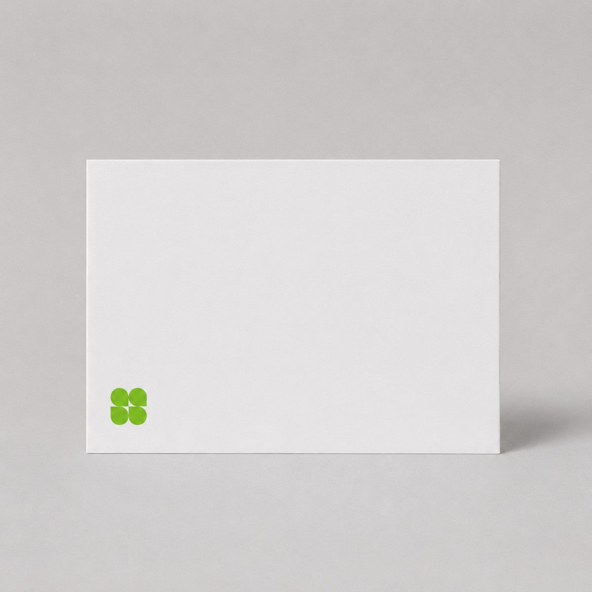 Stockka minimalist white 350gsm matte cardstock flat greeting card with a small green clover logo icon.