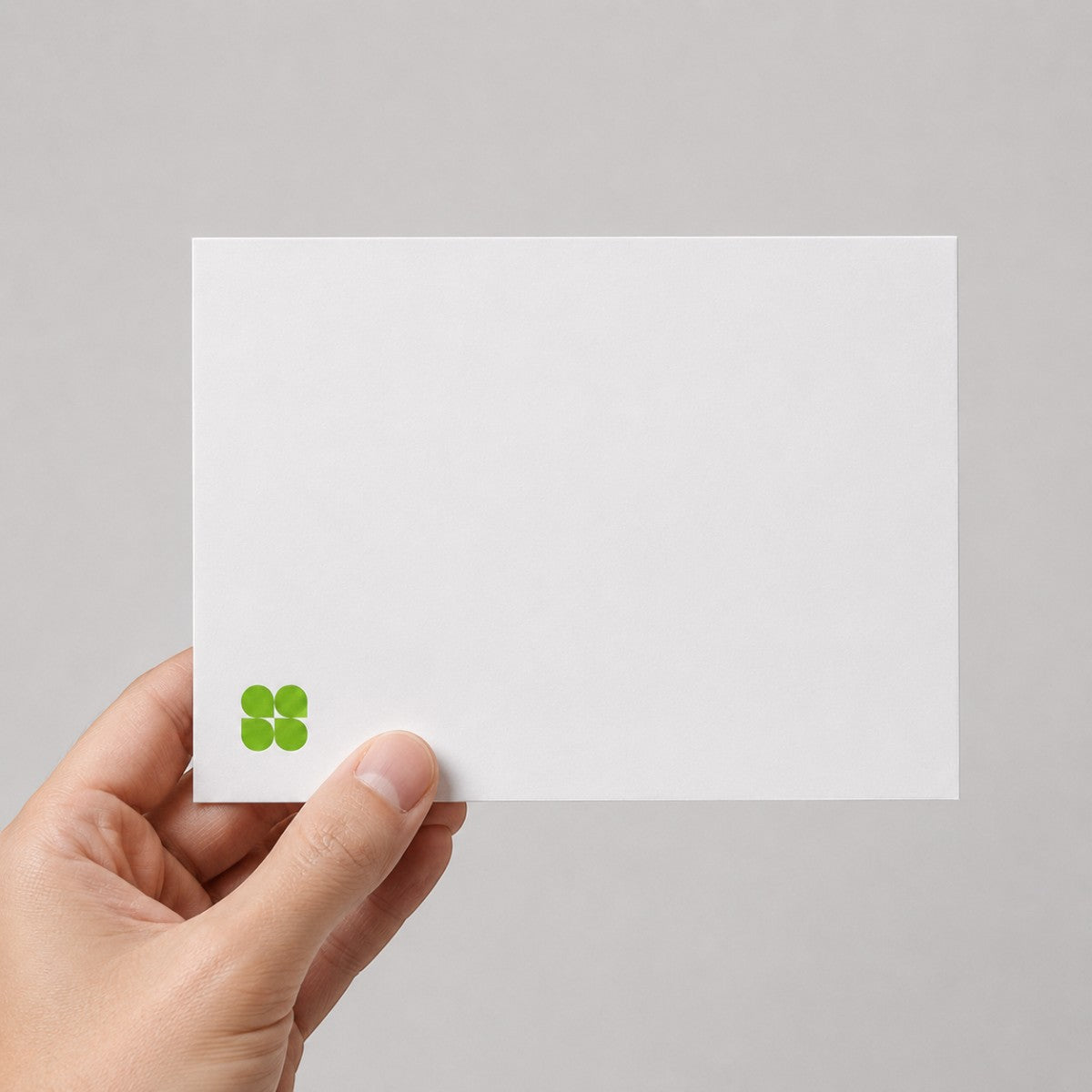 Stockka white matte 350gsm flat greeting card held in hand, featuring a minimalist green clover logo design.