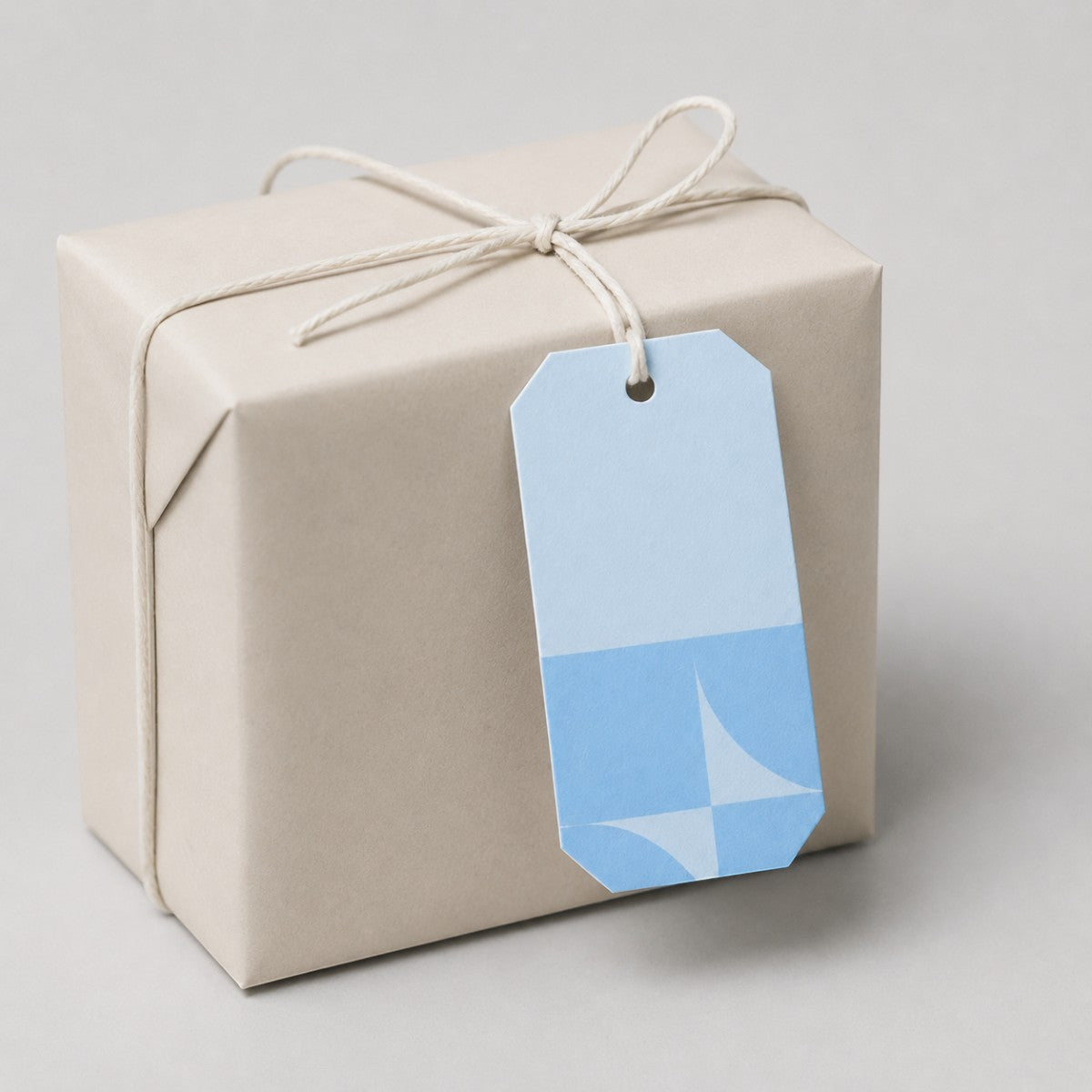 Stockka light blue gift tag with geometric pattern on a beige gift box tied with twine.
