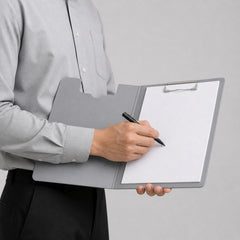 Stockka grey corrugated cardboard presentation folder with built-in clipboard, held by a person writing on a blank sheet.