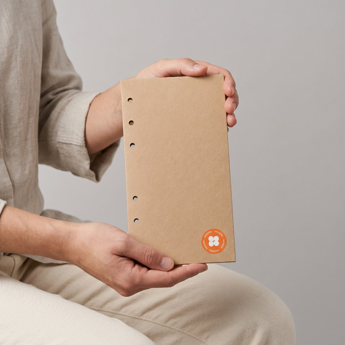 Stockka narrow brown kraft paper envelope with binder holes for filing, held by a person in a linen shirt.