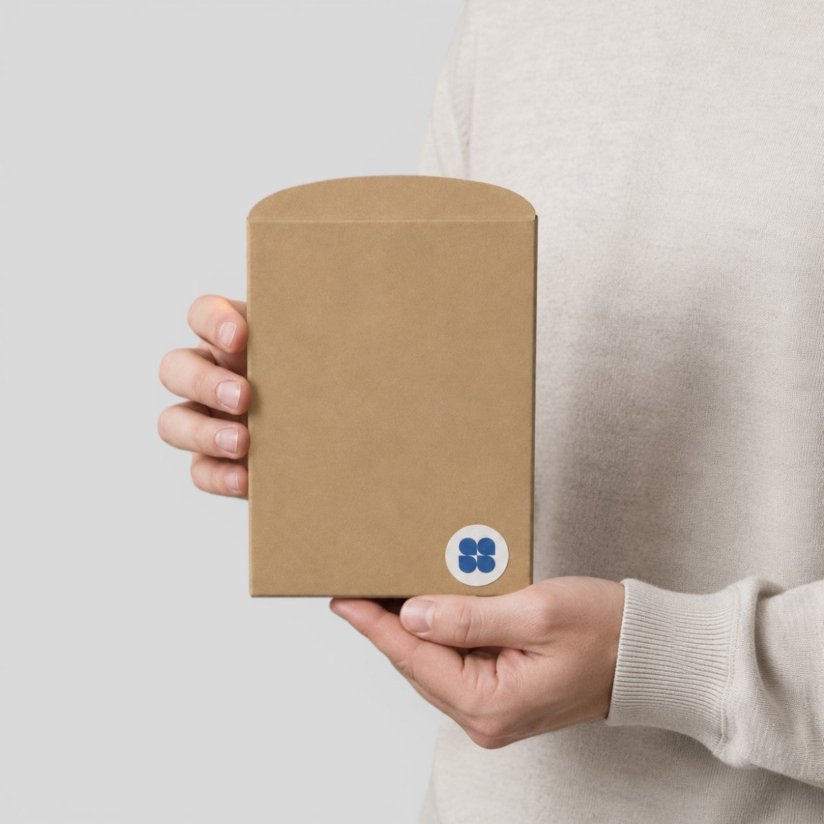 Stockka natural brown kraft paper pillow envelope with rounded flap, held by a person for gift or jewelry packaging.