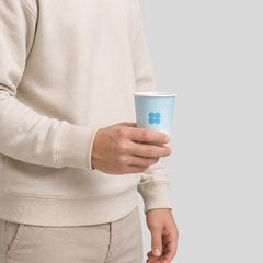 Stockka light blue paper cup with a blue logo, held by a person in a beige sweatshirt and tan pants.