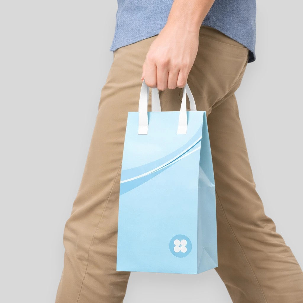Stockka light blue tall paper take-out bag with white handles and a wave design. Perfect for bottles or narrow packaging.