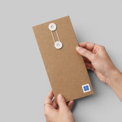 Stockka narrow brown kraft paper envelope with white string and disc closure held by hands