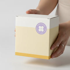 Stockka rigid cube gift box in pastel yellow and white with a purple circular logo. Ideal for luxury packaging.