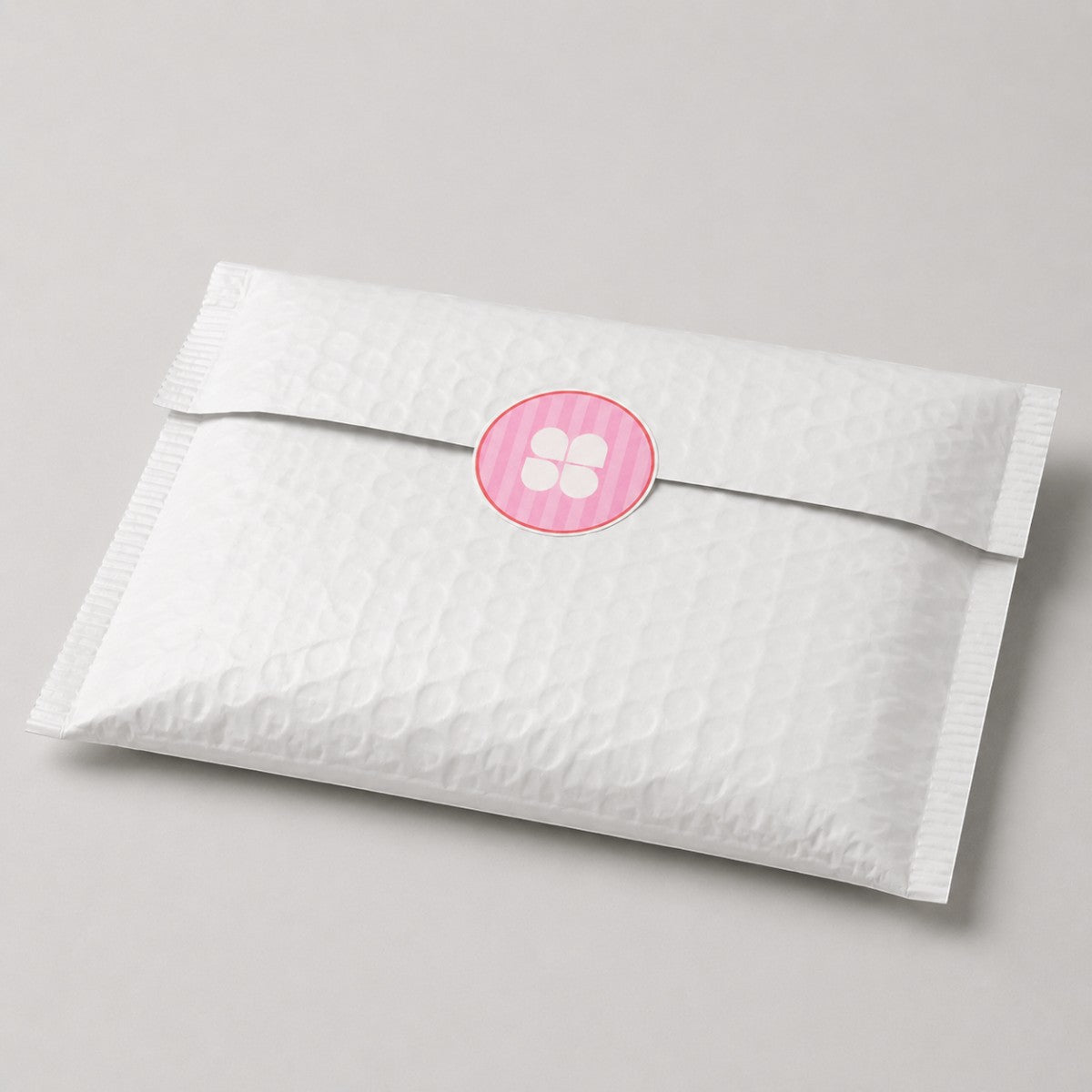 Stockka pink and white striped round sticker with a four-petal flower design on a white padded envelope.