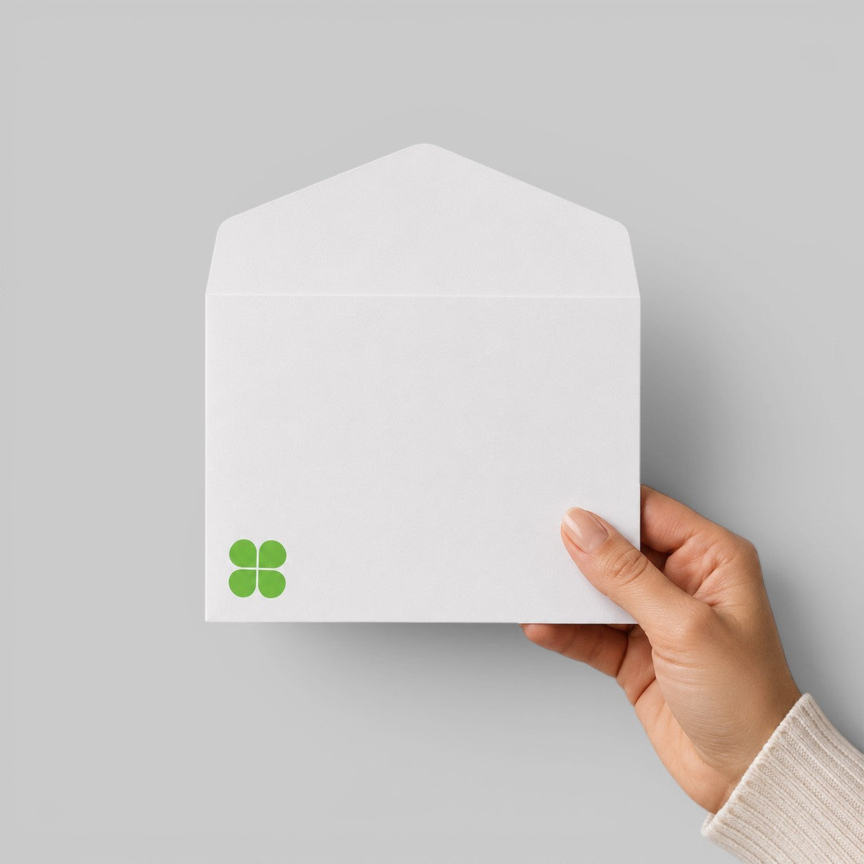 Stockka classic white envelope with triangular flap, 120gsm smooth paper, held by hand, featuring a green clover logo
