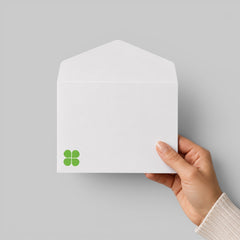 Stockka classic white envelope with triangular flap, 120gsm smooth paper, held by hand, featuring a green clover logo