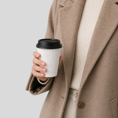 Stockka white paper coffee cup with corrugated texture and black lid, held by a person wearing a beige coat.