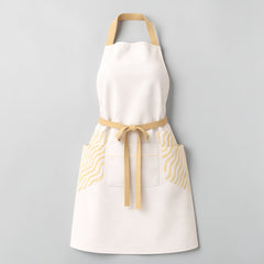 Stockka white full-length apron with tan straps, tan waist tie, and two side pockets featuring a yellow wavy stripe pattern. Made from cotton-polyester blend.