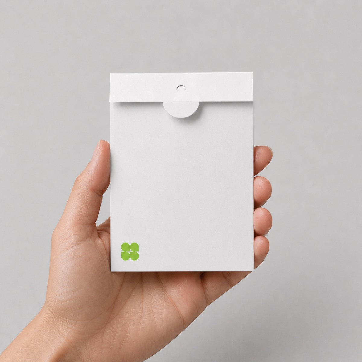 A hand holding a Stockka white matte 350g cardboard envelope with a circular thumb-lock closure for elegant invitations.