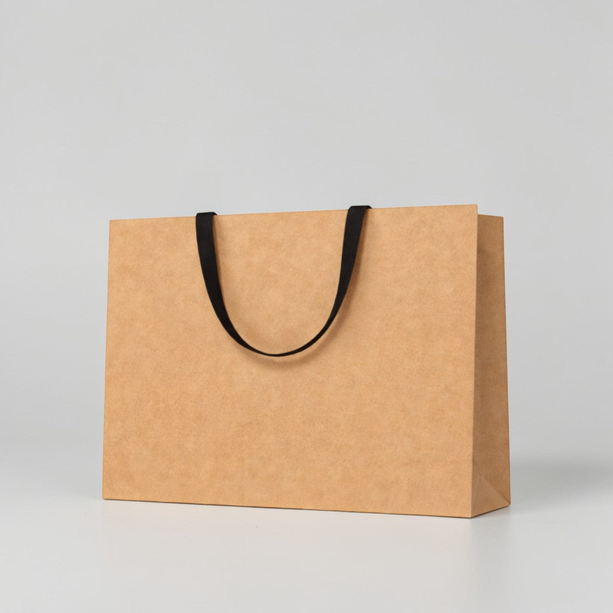 Stockka wide kraft paper gift bag with reinforced base and flat fabric handles, ideal for retail and premium packaging.